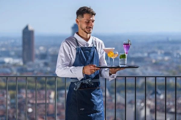 Serveur en tablier portant un plateau en terrasse, illustrant les contrats courts et saisonniers